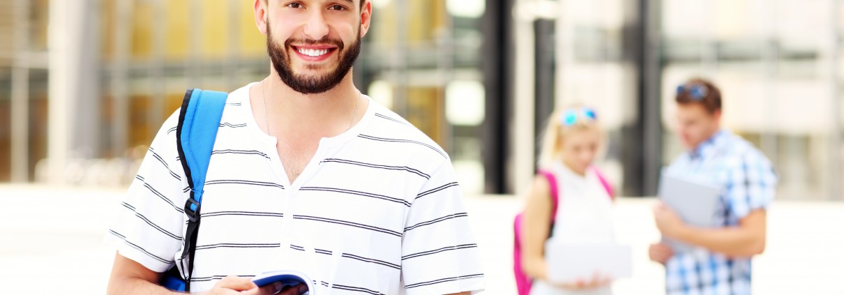 A picture of a young student standing and smiling in the campus