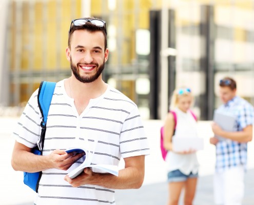 A picture of a young student standing and smiling in the campus