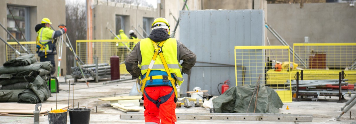 Rear view of male builder construction worker on building site wearing hard hat and hi-vis vest