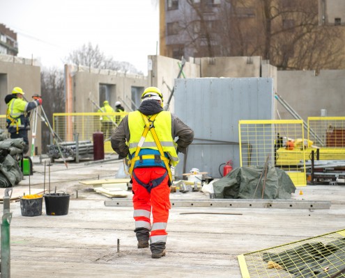 Rear view of male builder construction worker on building site wearing hard hat and hi-vis vest